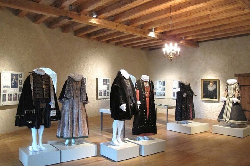 Mannequins displaying historical clothing in an indoor exhibit with wooden beams and a chandelier. 2