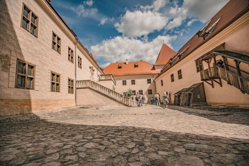 Une cour pavée de pierres, bordée de bâtiments historiques, avec un escalier et un ciel dégagé. 3