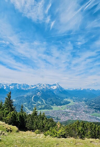 A mountain landscape with a town in the valley, clear skies, and snow-capped peaks. 1