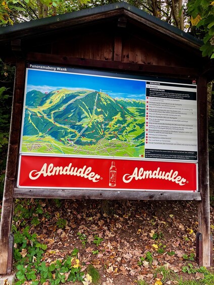 A mountain hiking trail map with a red Almdudler logo. 5