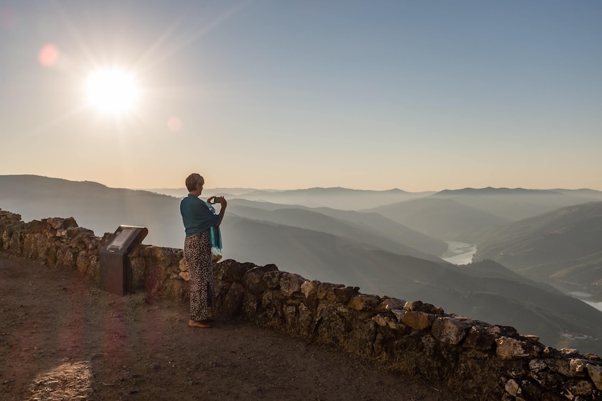 A person standing on a stone wall overlooking a valley with a river. 3