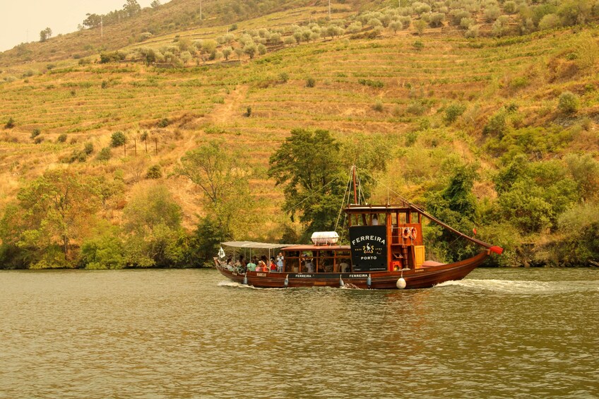 A boat named 'FERRERA' with passengers, on a river with a hilly landscape in the background. 4