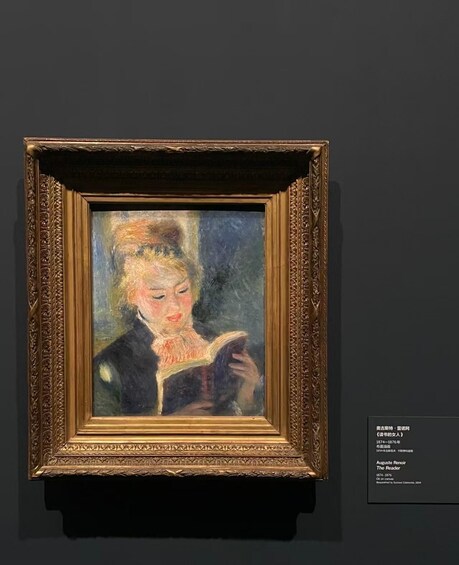 A framed painting of a woman reading a book, with a detailed ornate frame and a label with text. 3