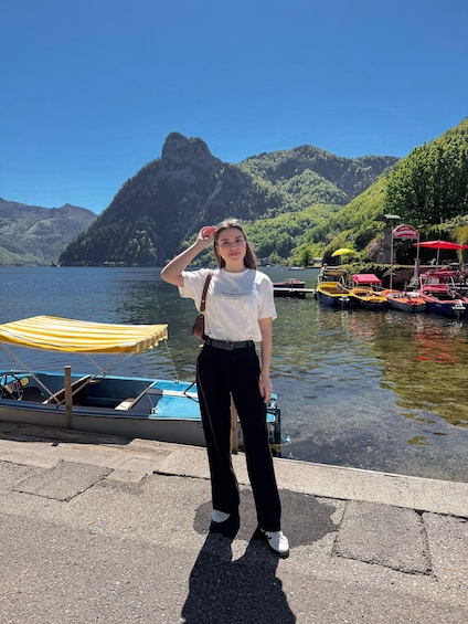 A person standing by a lake with boats, a mountain, and a red sign. 4