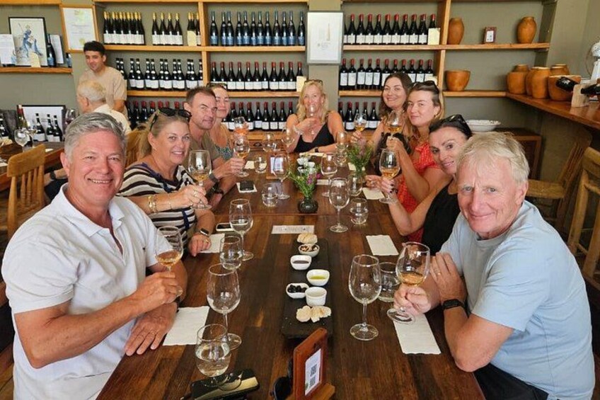 A group of people sitting around a table with wine glasses, in a room with shelves of wine bottles. 1