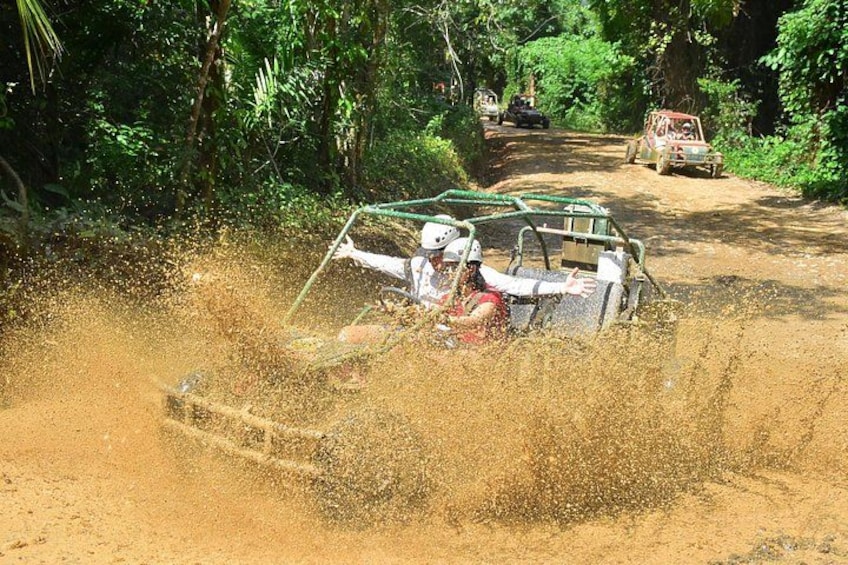 A vehicle driving through a muddy path, kicking up dust. 4