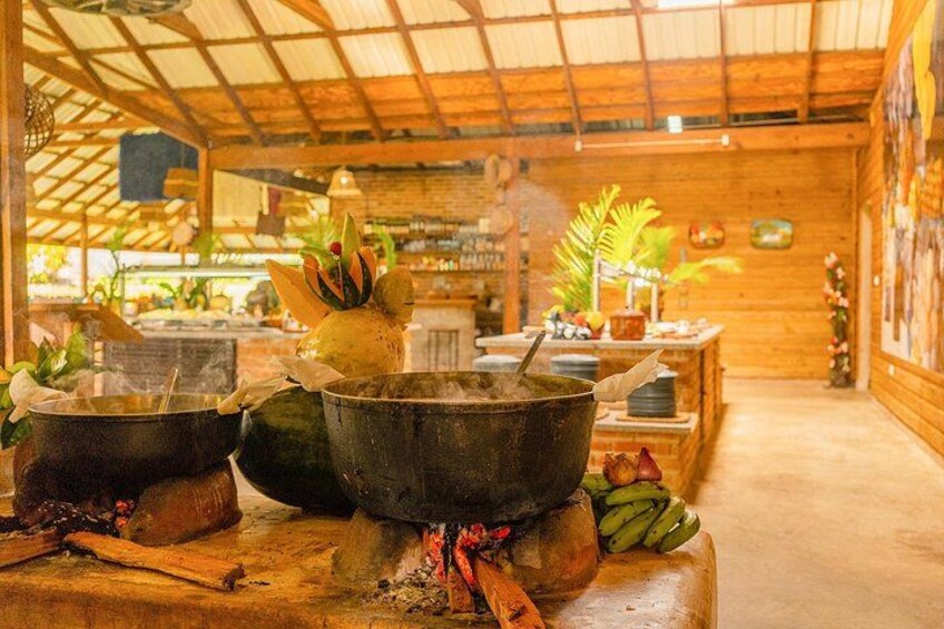 Una cocina rústica con ollas grandes sobre una estufa, paredes de madera y un techo de paja. 4