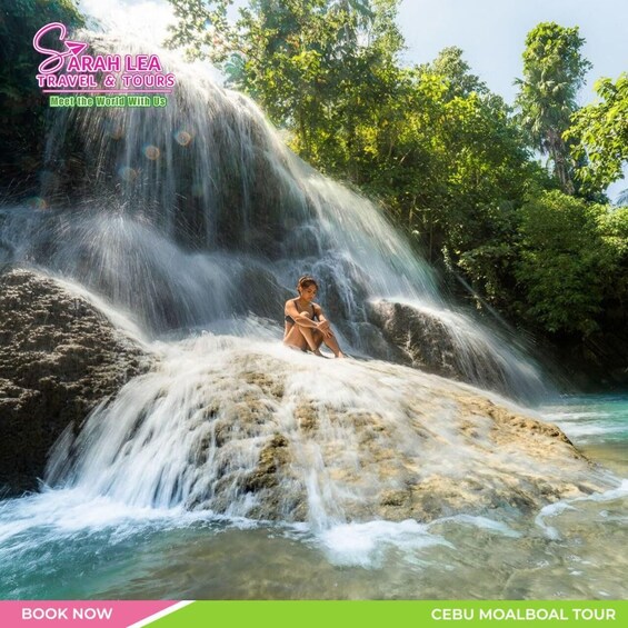 A waterfall with a person sitting on a rock, surrounded by lush greenery. 2