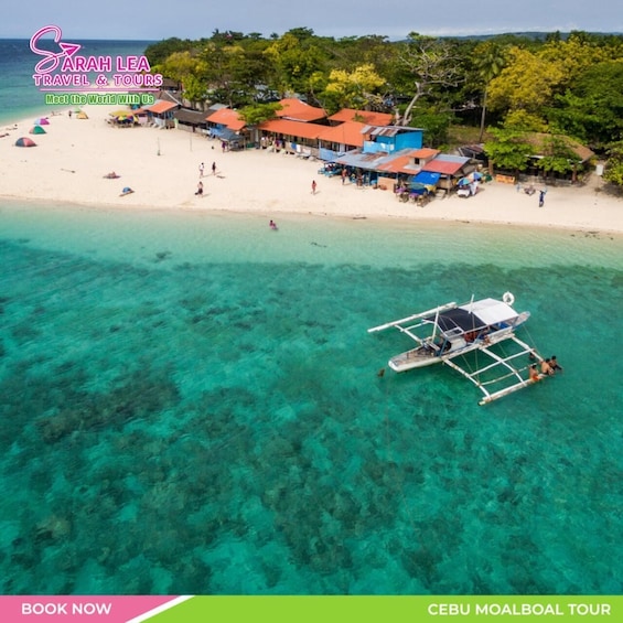 A beach with clear turquoise water, a boat, and a village with colorful houses. 1