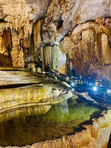 A cave with stalactites, a water stream, and a wooden walkway. 3