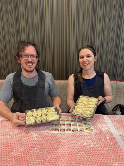 Two people holding trays of dumplings at a table with a menu. 3
