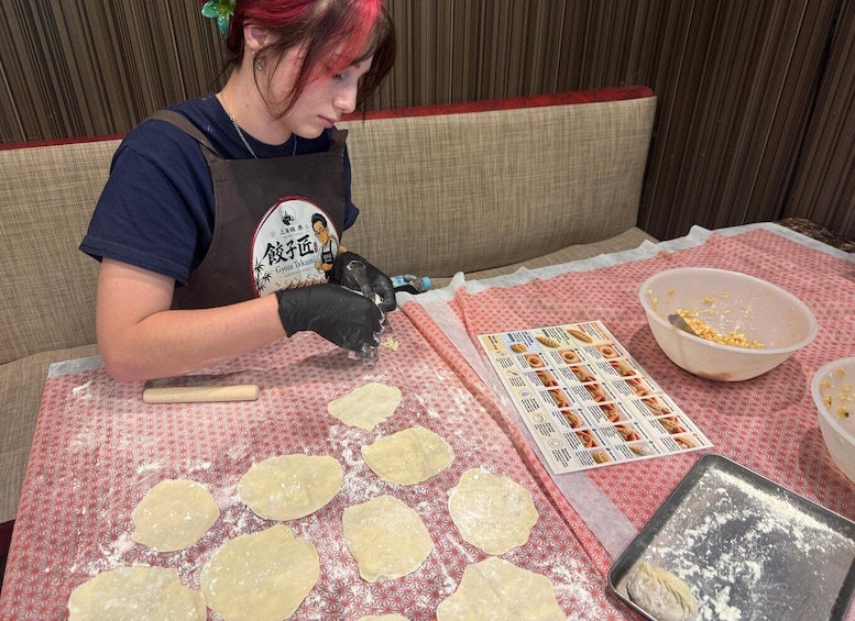 A person preparing food, specifically dough, on a table with a patterned tablecloth. 4