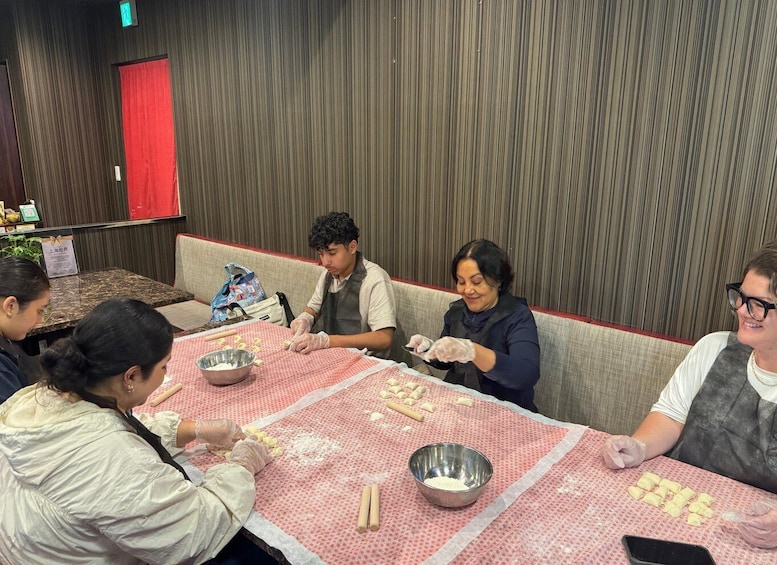 A group of people engaged in a cooking activity, using rolling pins and bowls on a table covered with a patterned cloth. 2