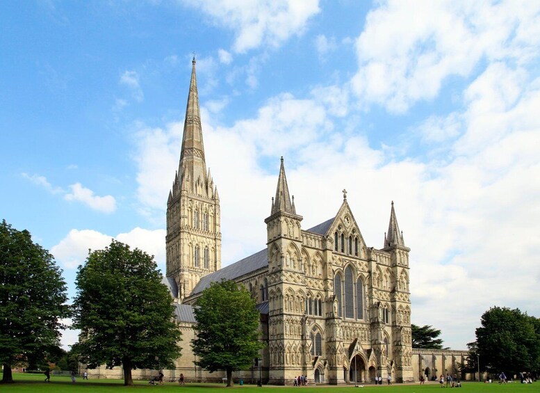 A large Gothic-style cathedral with a prominent spire and multiple towers, surrounded by a green park with trees and people. 5