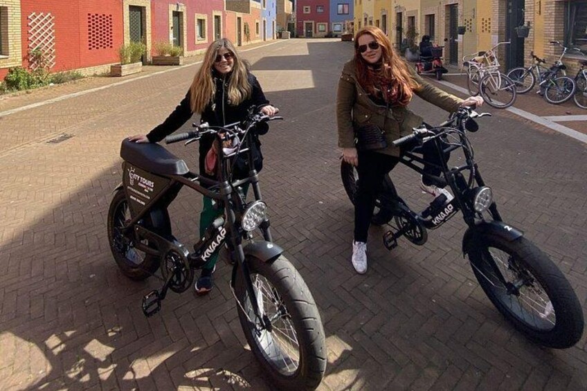 Two people standing next to electric scooters on a paved street with buildings in the background. 4