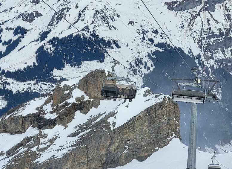 A cable car ascending a snowy mountain with rocky terrain and forested slopes. 3