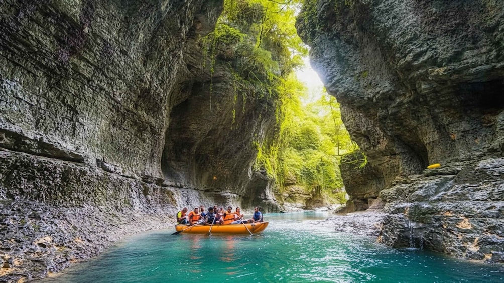 A group of people in a yellow raft navigating through a narrow, rocky canyon with turquoise water. 5