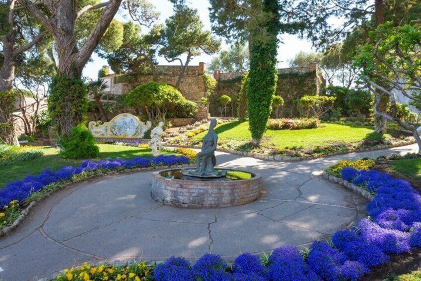 A garden with a circular fountain, surrounded by blue and yellow flowers, and a statue. 2