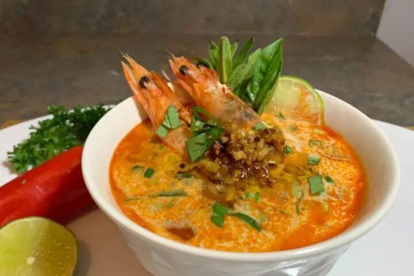 A bowl of soup with shrimp, lime, and herbs. 1