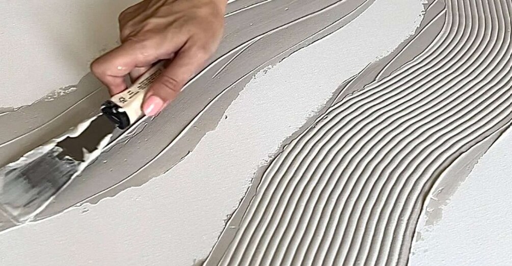 A hand applying textured plaster to a wall. 2