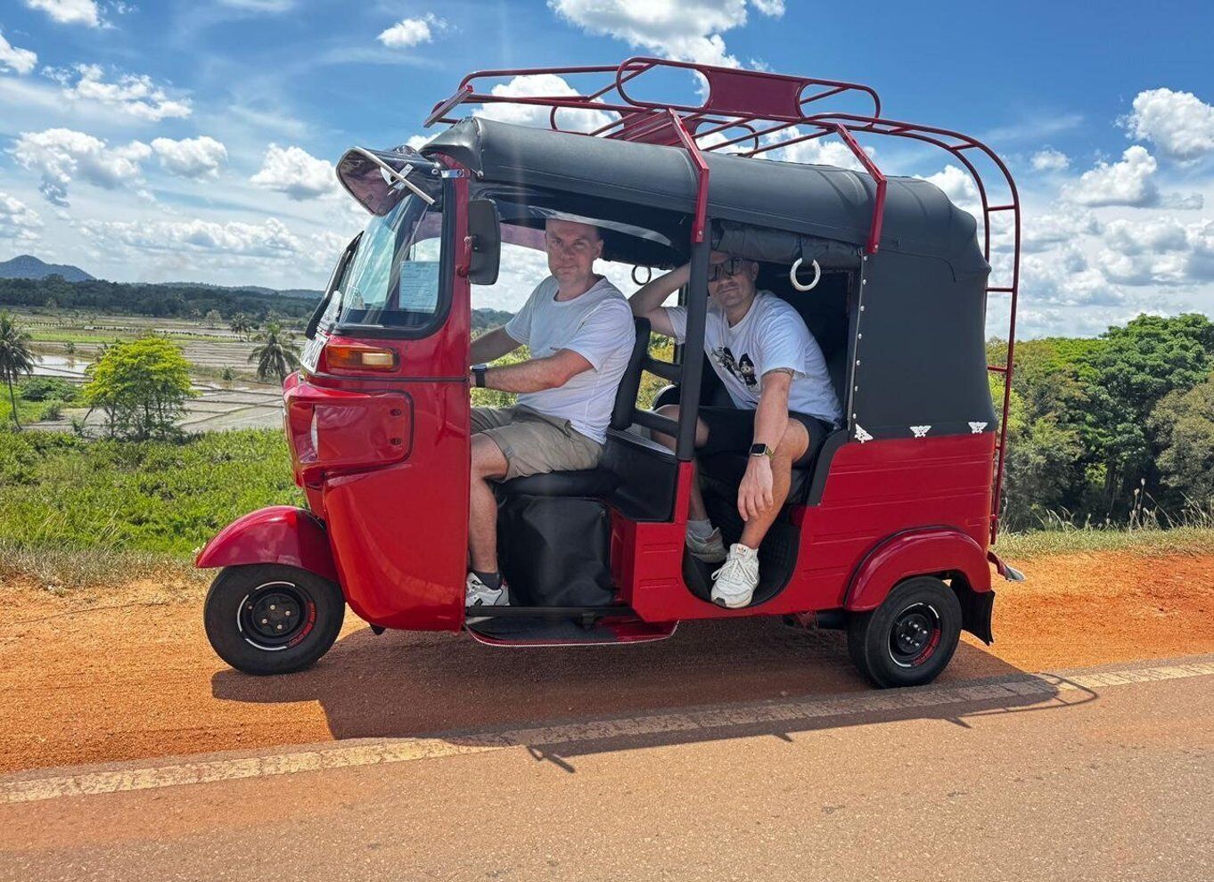 A red auto-rickshaw on a road with a rural landscape in the background. 5