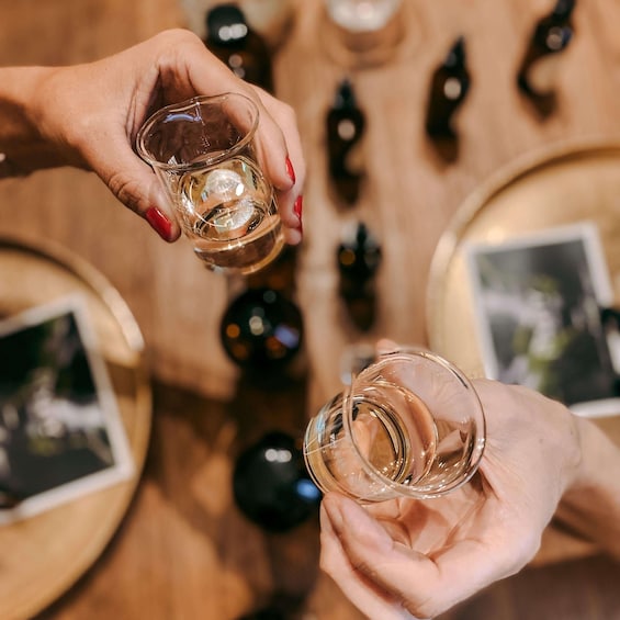 Two hands holding clear glasses, a wooden table with black decorative items, and a blurred background. 1