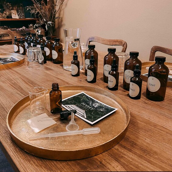 A wooden table with various bottles labeled with names, a tray with a card and droppers, and a glass container. 3