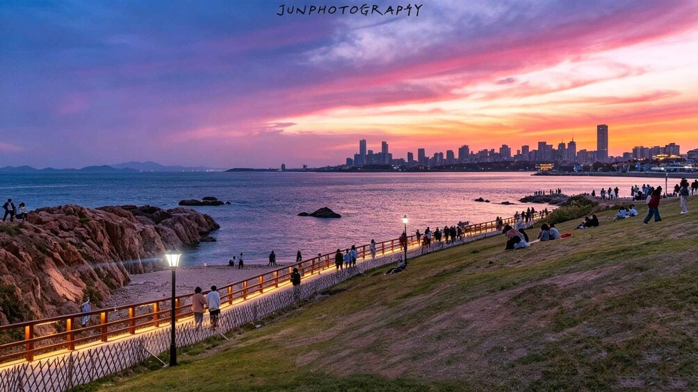 A sunset over a coastal city with a park, people, and a city skyline. 4