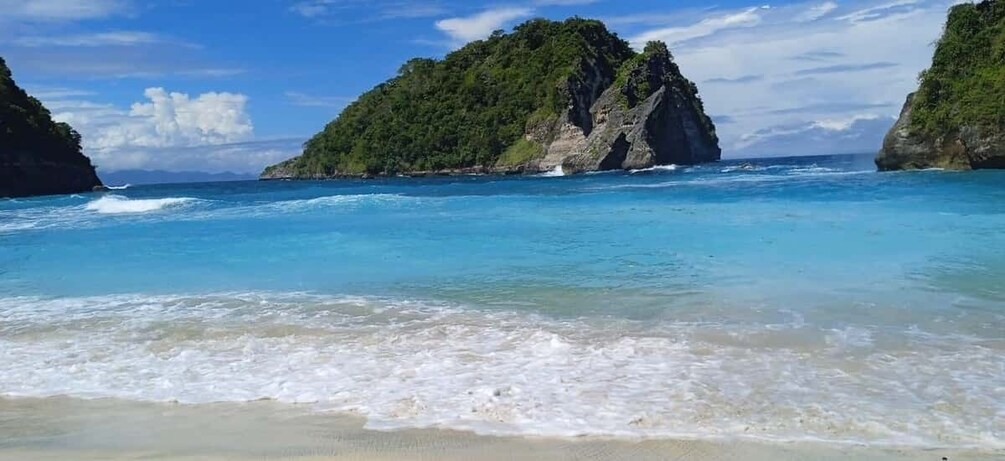 A beach with clear turquoise water, white sand, and two green, rocky islands in the distance. 2