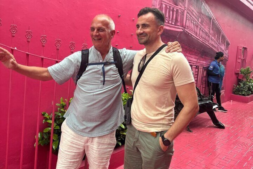 Dos personas frente a una pared rosa con balcón. 3