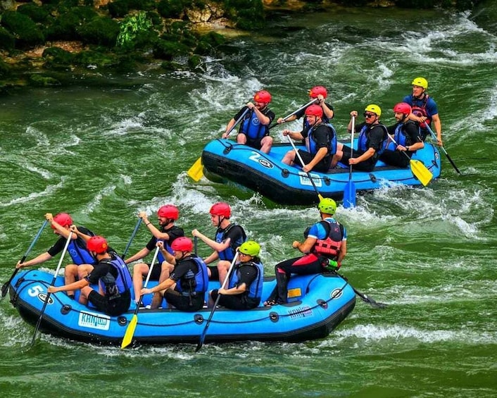 Two blue inflatable rafts on a river with people wearing helmets and life jackets. 1