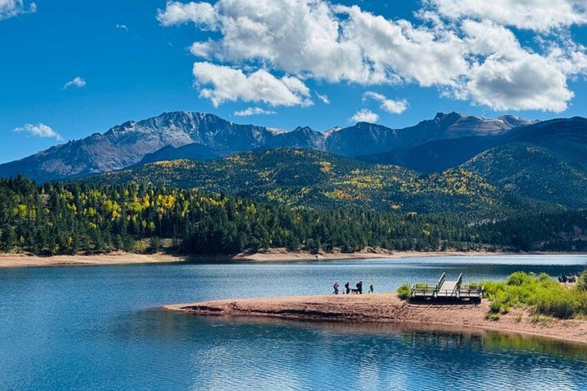 A lake with mountains in the background, a sandy beach, and a small dock with people. 1