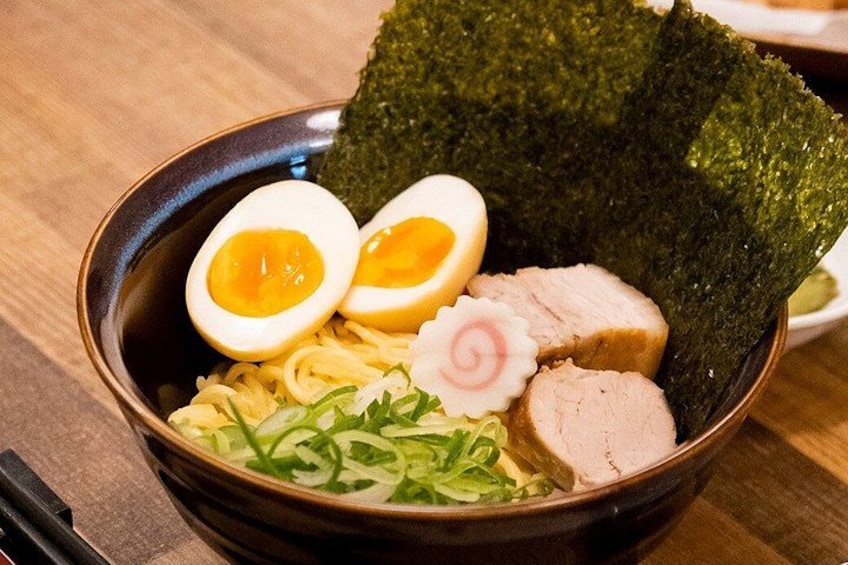 A bowl of ramen with sliced pork, boiled egg, seaweed, and green onions. 2