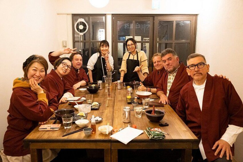 A group of people seated around a wooden table with various dishes and drinks. 4