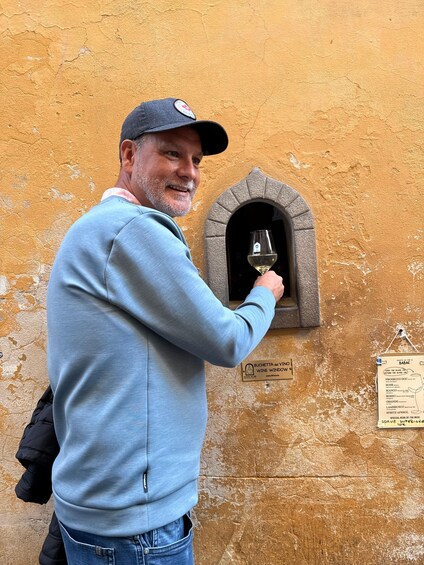A man holding a wine glass in front of a wine window with a sign indicating it is a wine cellar. 5