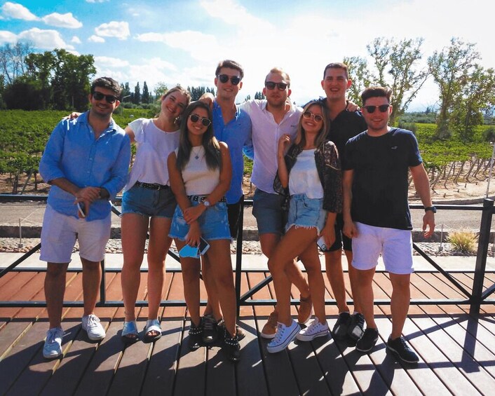 A group of people standing on a wooden deck with a vineyard in the background. 5