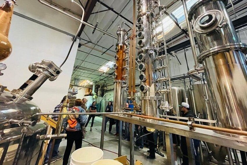 Un grand appareil de distillation industrielle, doté de plusieurs colonnes et de tuyaux, entouré de cuves en acier inoxydable, et sur lequel travaille une personne. 3