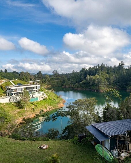 A lakeside property with a modern house, lush greenery, and a clear sky. 2