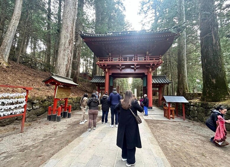 A traditional Japanese torii gate in a forested area with visitors. 2