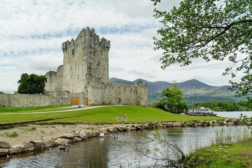 Un castillo histórico junto a un lago, con un primer plano de césped y montañas al fondo. 3