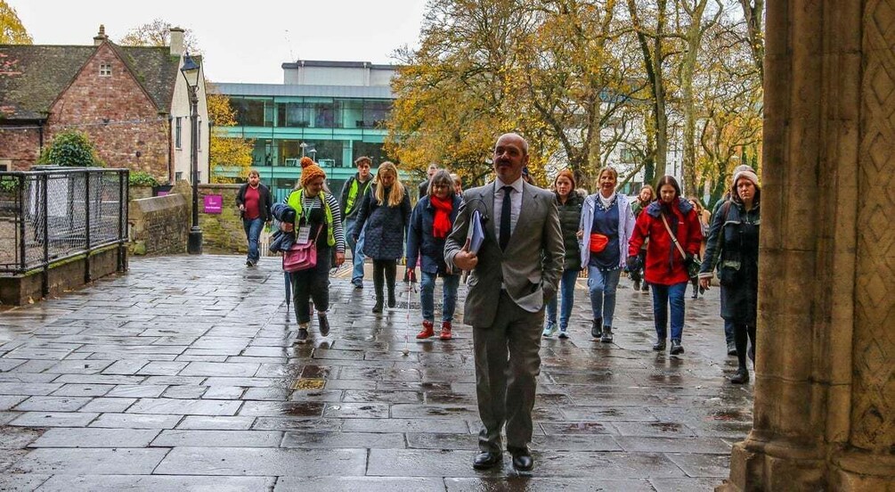 A group of people walking on a wet cobblestone path in an urban setting with buildings and trees in the background. 4