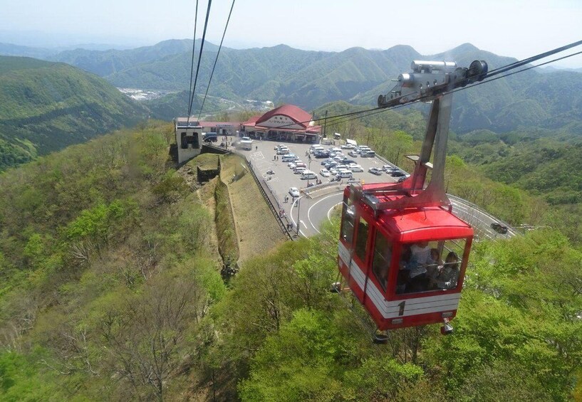 A red cable car ascending a mountain with a parking lot and a building in the background. 2
