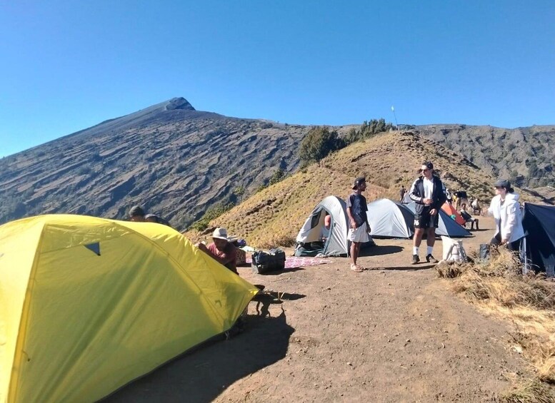 A group of people camping near a mountain with tents and a yellow tent on a dirt path. 2