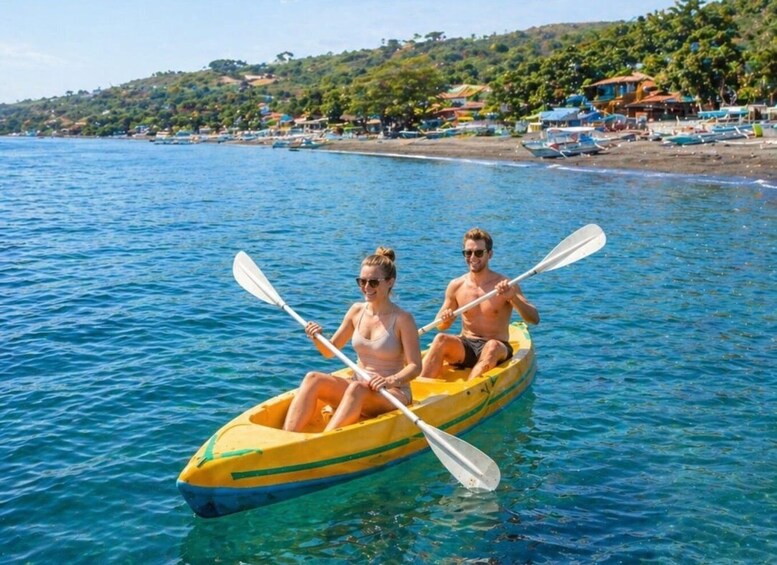 Two people kayaking on a calm sea with a beach and houses in the background. 4