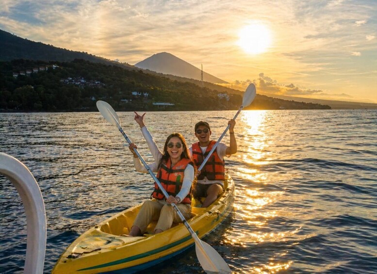 Two people kayaking on a calm lake with a sunset in the background. 1