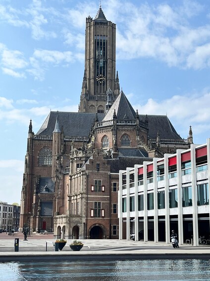 A historic building with a clock tower, a modern glass extension, and a water feature in front. 1