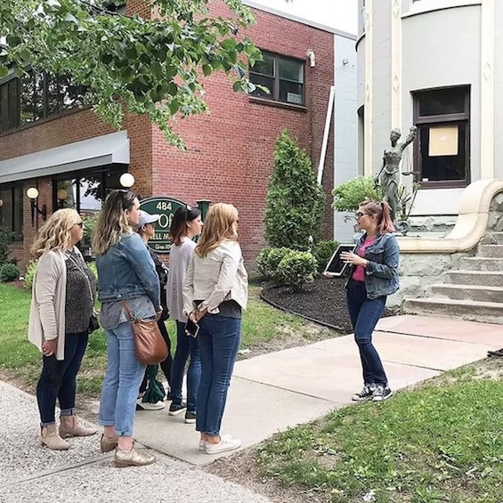 A group of people standing on a sidewalk in front of a building with a brick facade and a statue. 4