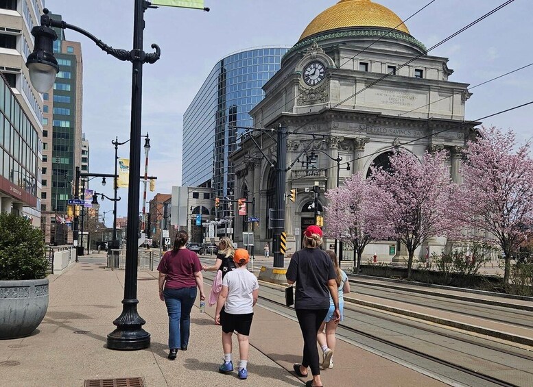 A city street with pedestrians, a historic building with a golden dome, and modern skyscrapers. 1