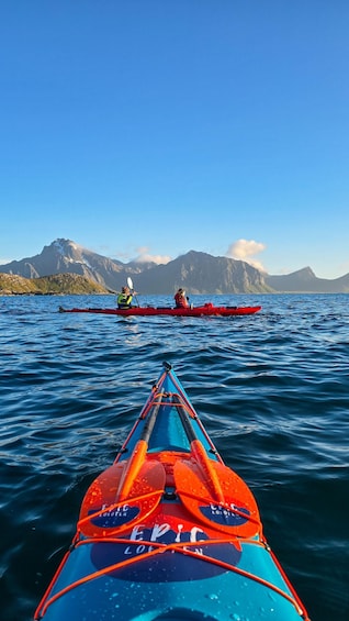 A kayak with 'EPIC' written on it, approaching a red kayak on the water with mountains in the background. 2