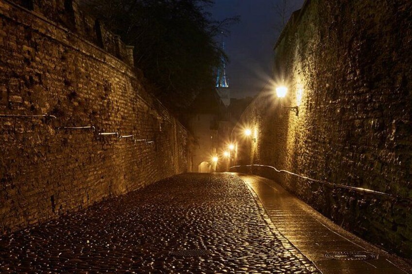 A cobblestone street at night with stone walls and street lamps. 3
